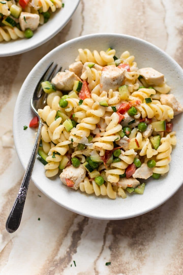 creamy chicken pasta primavera with fresh vegetables in white bowl with a fork