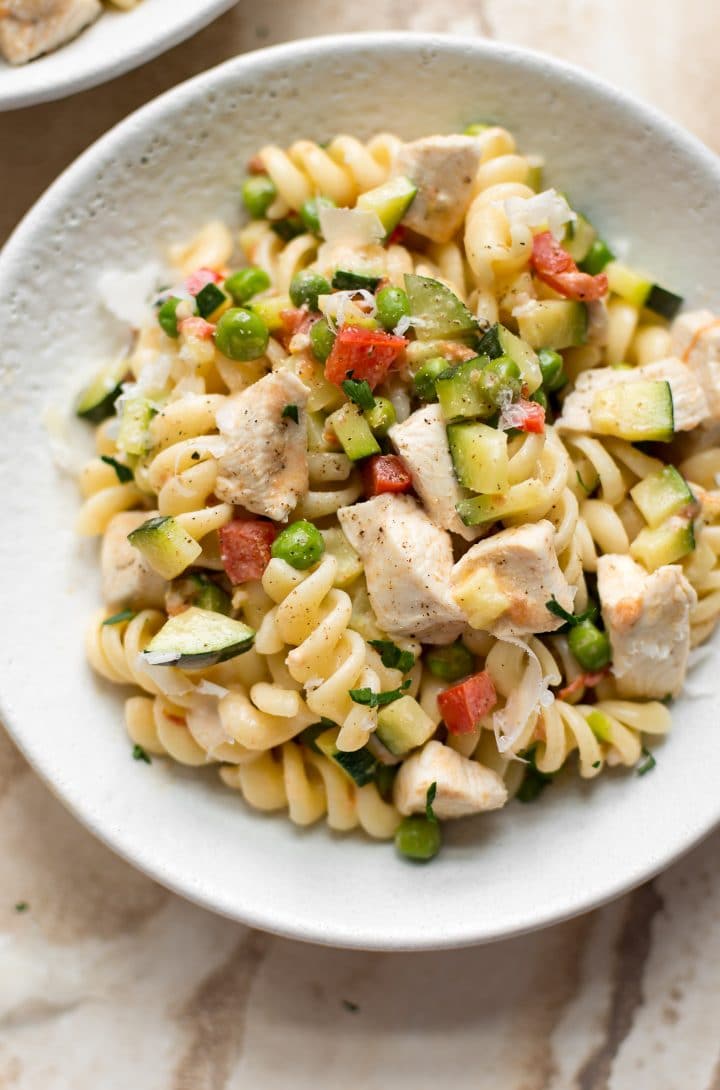 close-up of creamy Pasta Primavera with chicken and fresh vegetables in a white bowl
