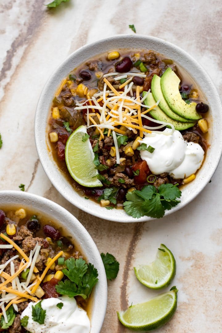 crockpot taco soup in two white bowls beside lime wedges