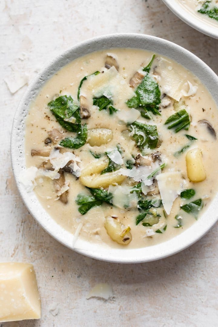 a white bowl with easy creamy spinach gnocchi soup with plenty of mushrooms, garlic, and parmesan cheese