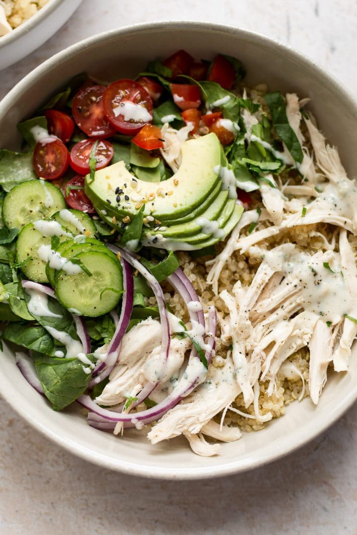 white bowl of ranch chicken quinoa salad with avocado, red onion, tomatoes, cucumber, and a homemade ranch dressing