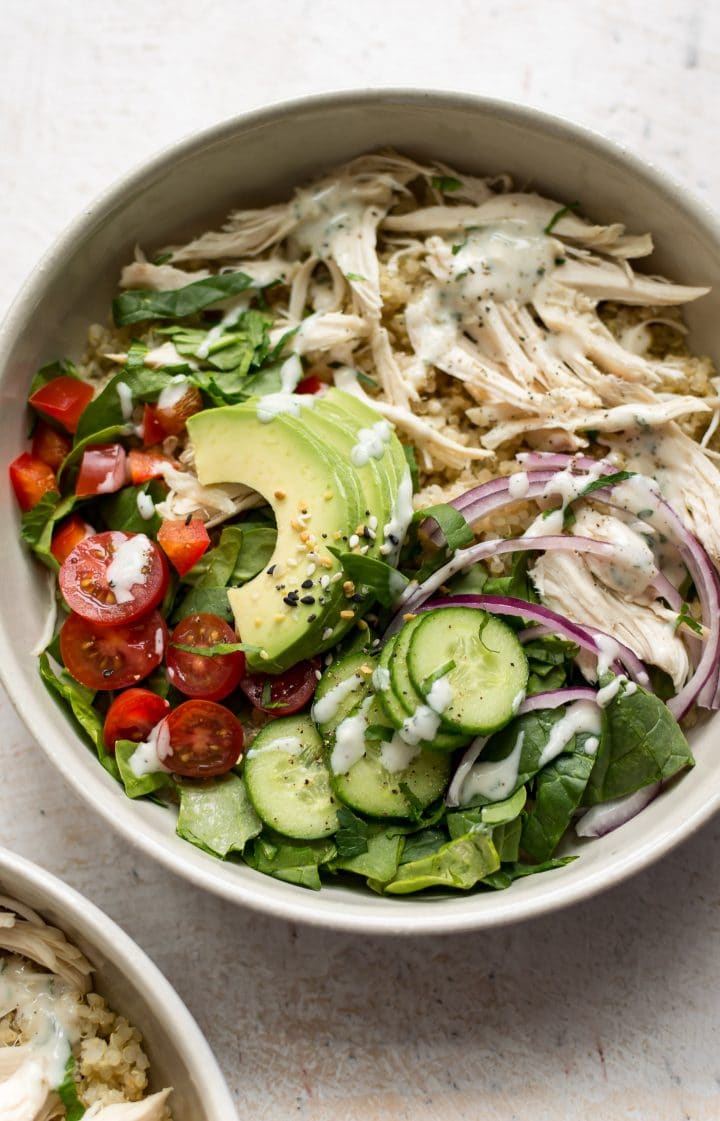 close-up of cold chicken quinoa salad with avocado slices, shredded chicken, little tomato, and cucumber in a bowl