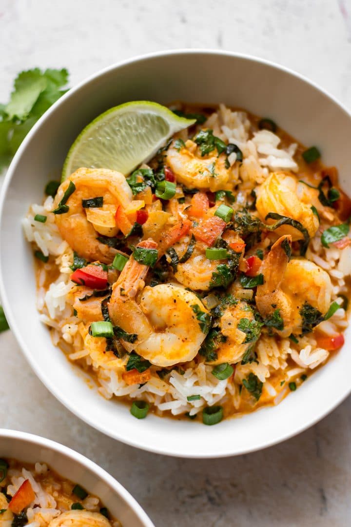 white bowl with close-up of Thai coconut shrimp curry over rice with a lime wedge