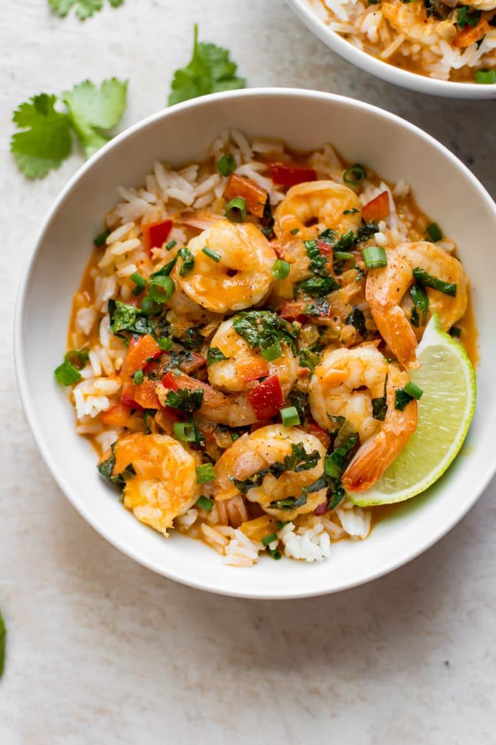 white bowl of Thai red shrimp curry over rice with lime wedge