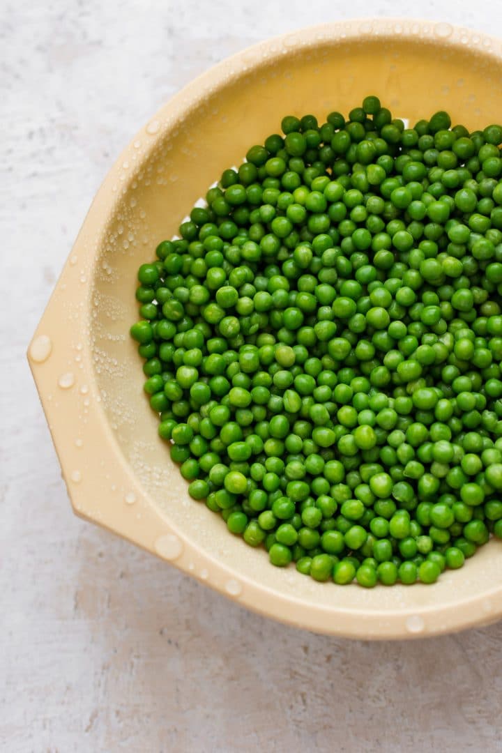 Frozen peas thawing in a colander