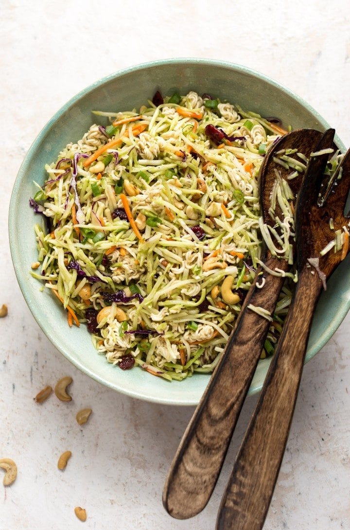 Broccoli ramen slaw in a blue salad bowl with salad tongs