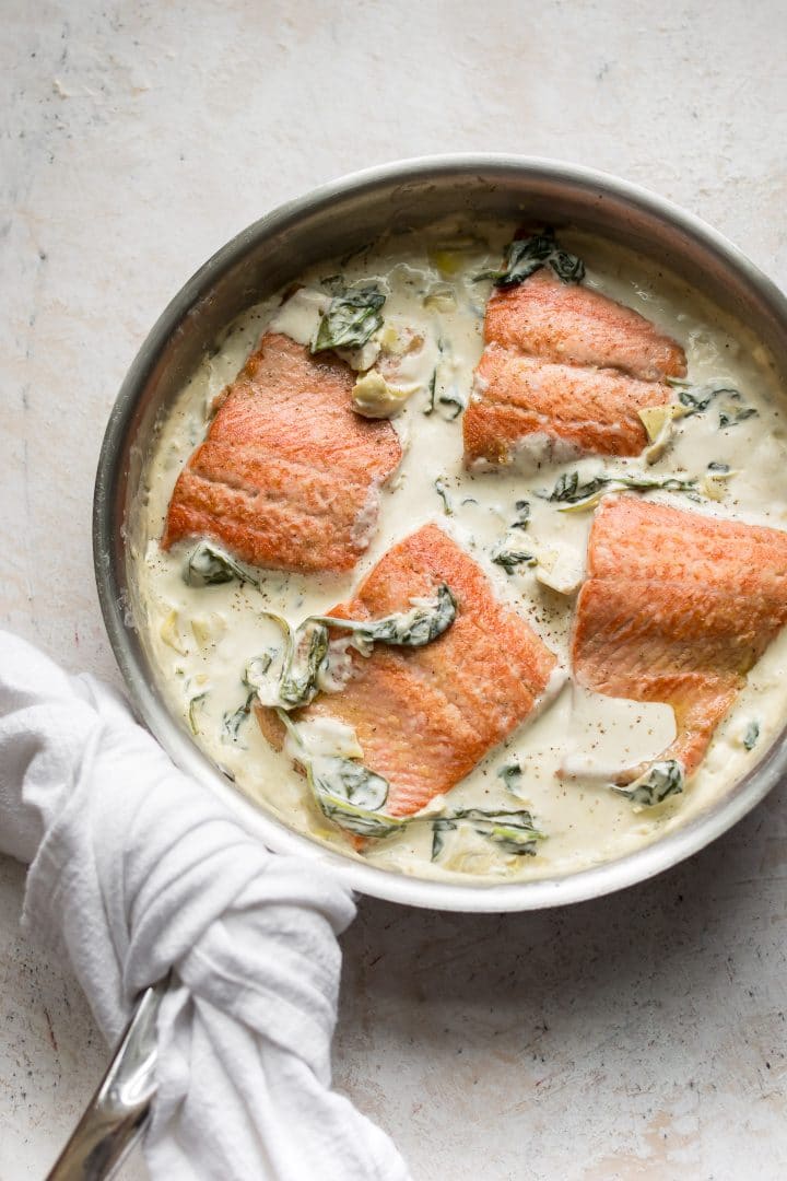 salmon in a creamy spinach and artichoke sauce in a skillet