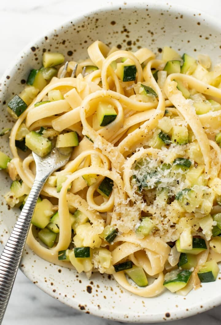 a bowl of pasta with zucchini sauce and a fork