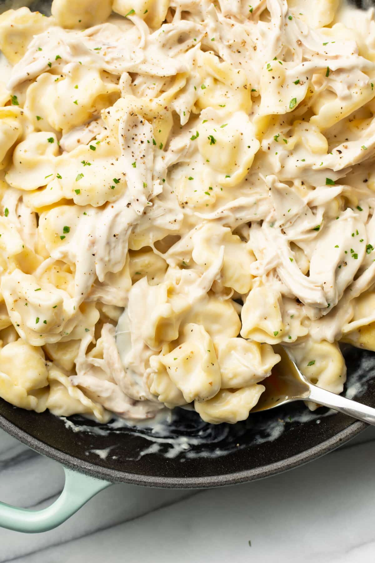 closeup of a skillet with chicken tortellini in alfredo sauce and a serving spoon