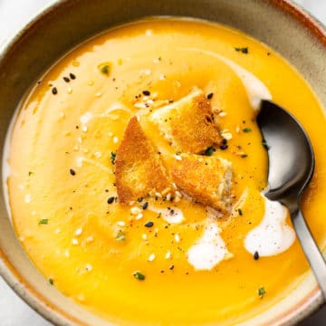 the best butternut squash soup with coconut milk (in a bowl with a spoon, on a marble background, topped with croutons)