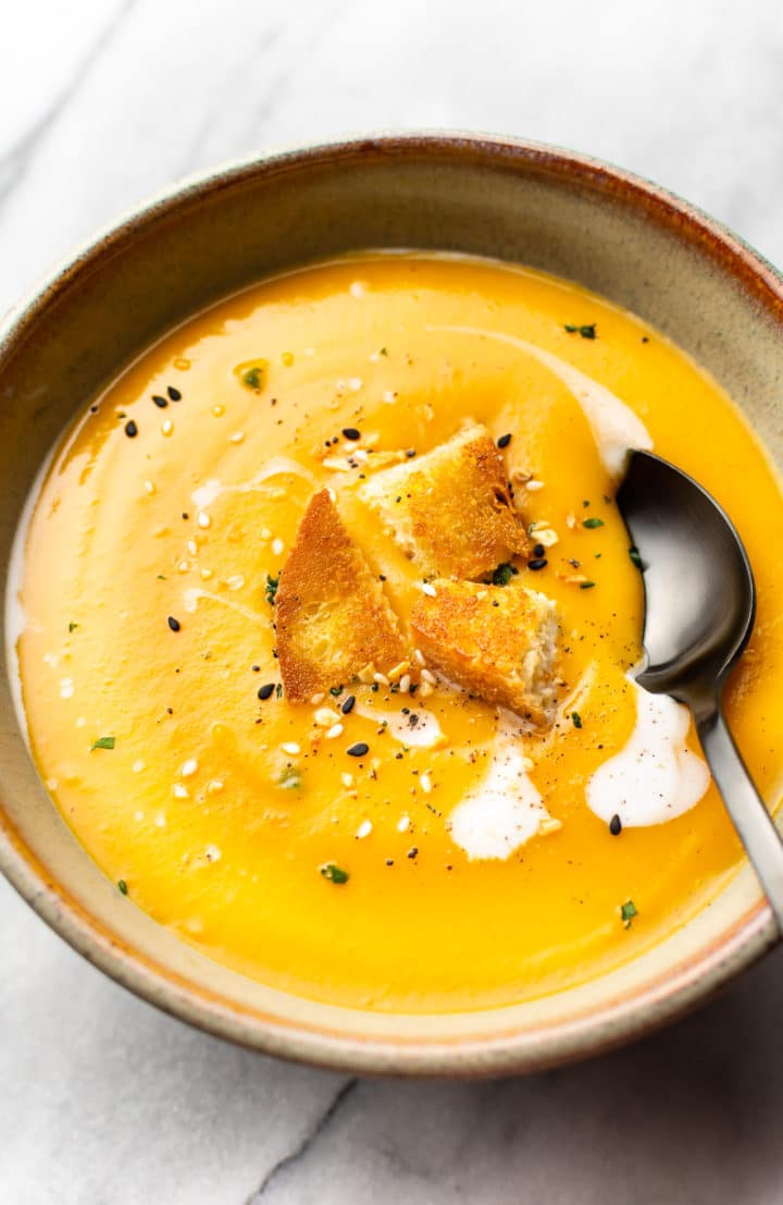 the best butternut squash soup with coconut milk (in a bowl with a spoon, on a marble background, topped with croutons)