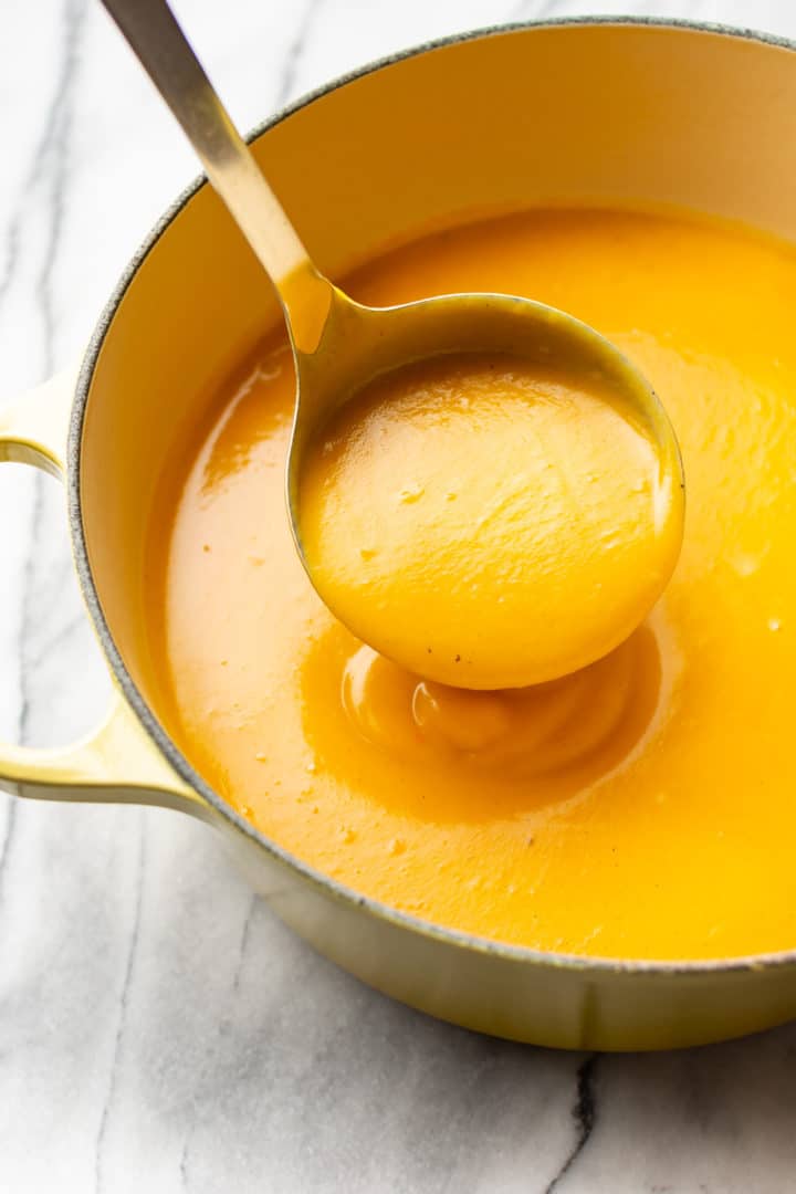 the best butternut squash soup in a yellow soup pot with a ladle full of soup