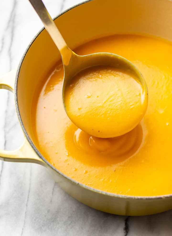 the best butternut squash soup in a yellow soup pot with a ladle full of soup