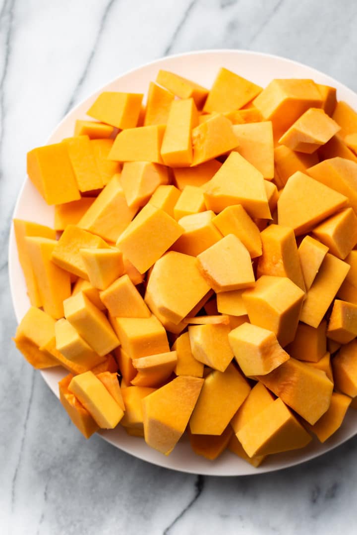 chopped raw butternut squash on a white plate and marble background