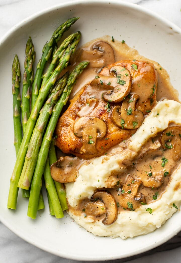 chicken marsala on a plate with mashed potatoes and asparagus