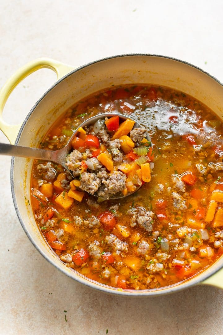 sausage and sweet potato soup in a yellow pot with a ladle of soup