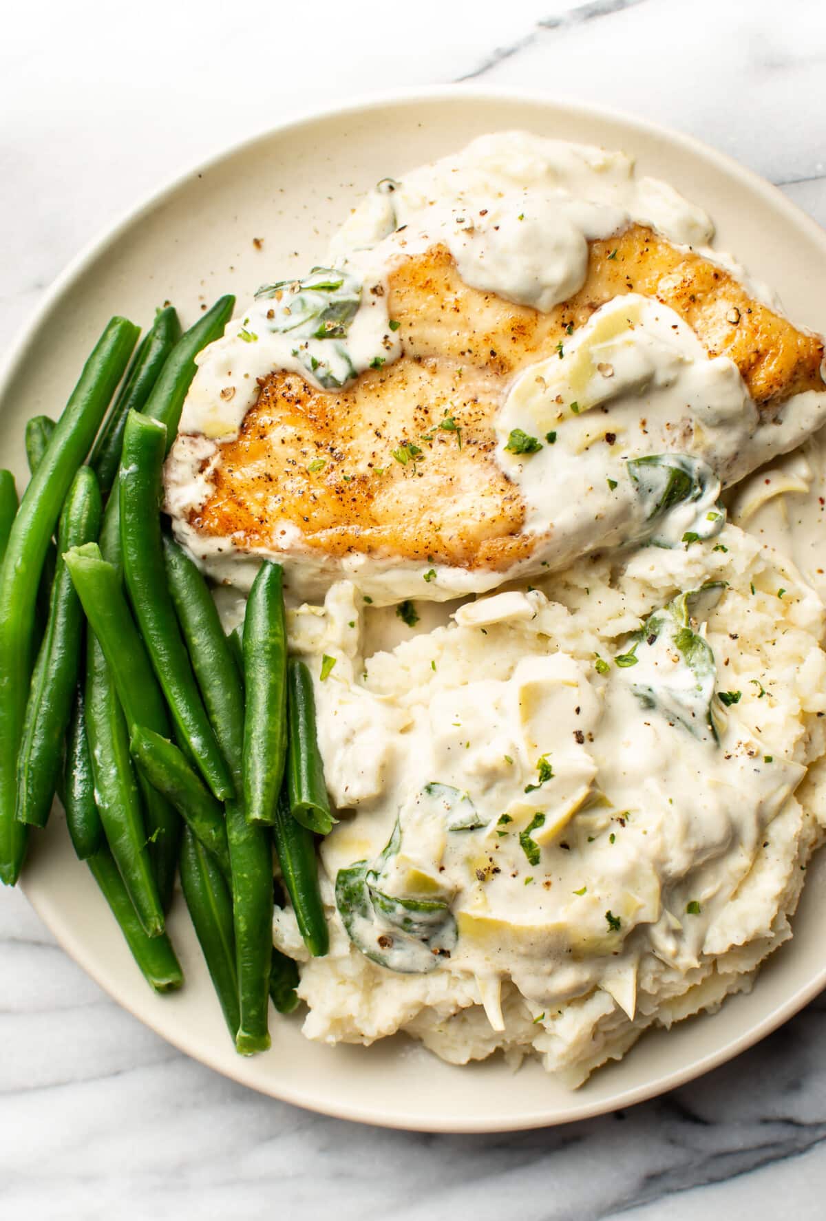 a plate with spinach artichoke chicken, green beans, and mashed potatoes