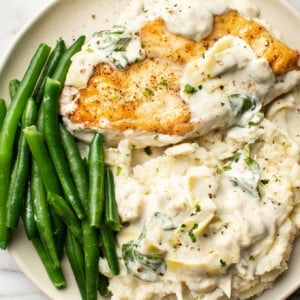 a plate with spinach artichoke chicken, green beans, and mashed potatoes