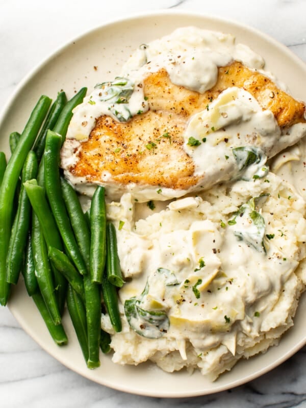 a plate with spinach artichoke chicken, green beans, and mashed potatoes