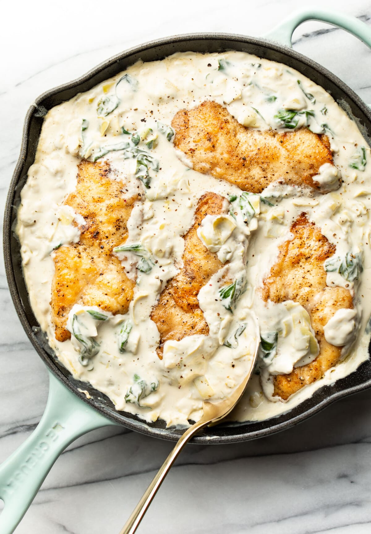 a skillet with spinach artichoke chicken and a serving spoon