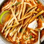 a bowl of chicken tortilla soup with a lime wedge and spoon