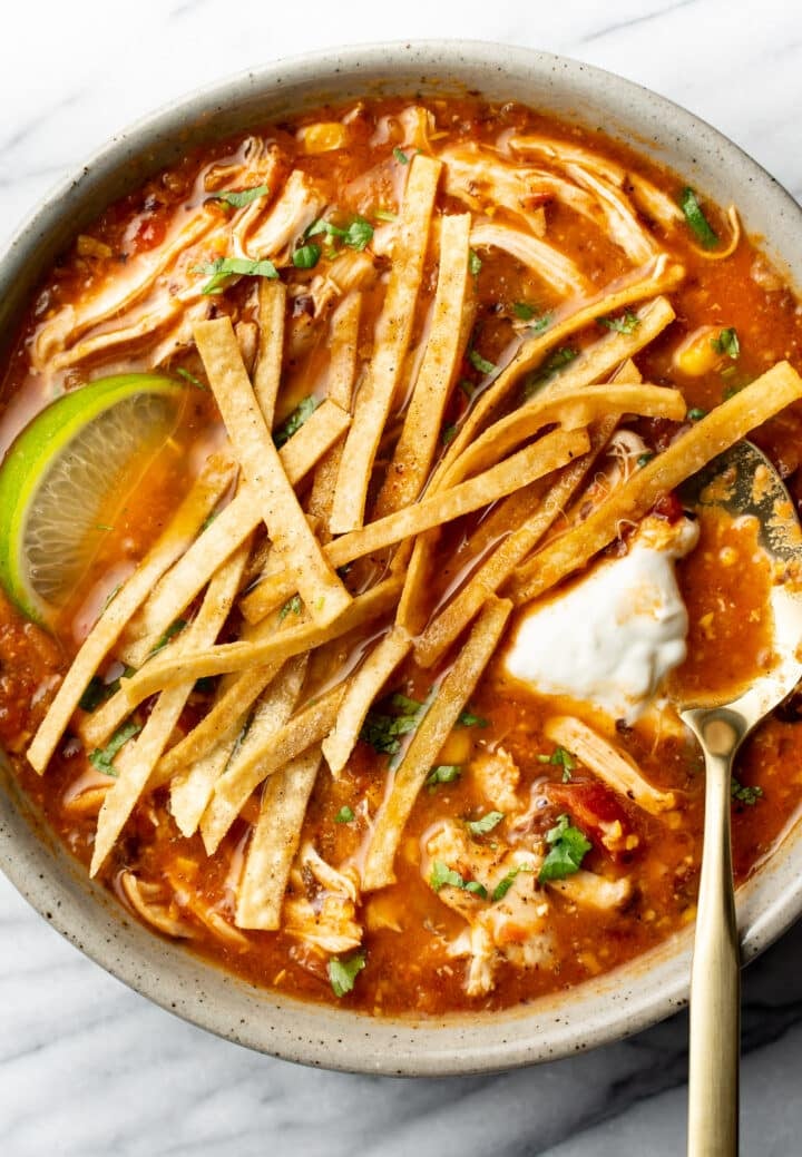 a bowl of chicken tortilla soup with a lime wedge and spoon