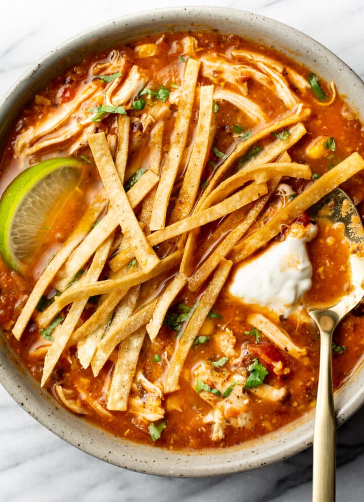 a bowl of chicken tortilla soup with a lime wedge and spoon