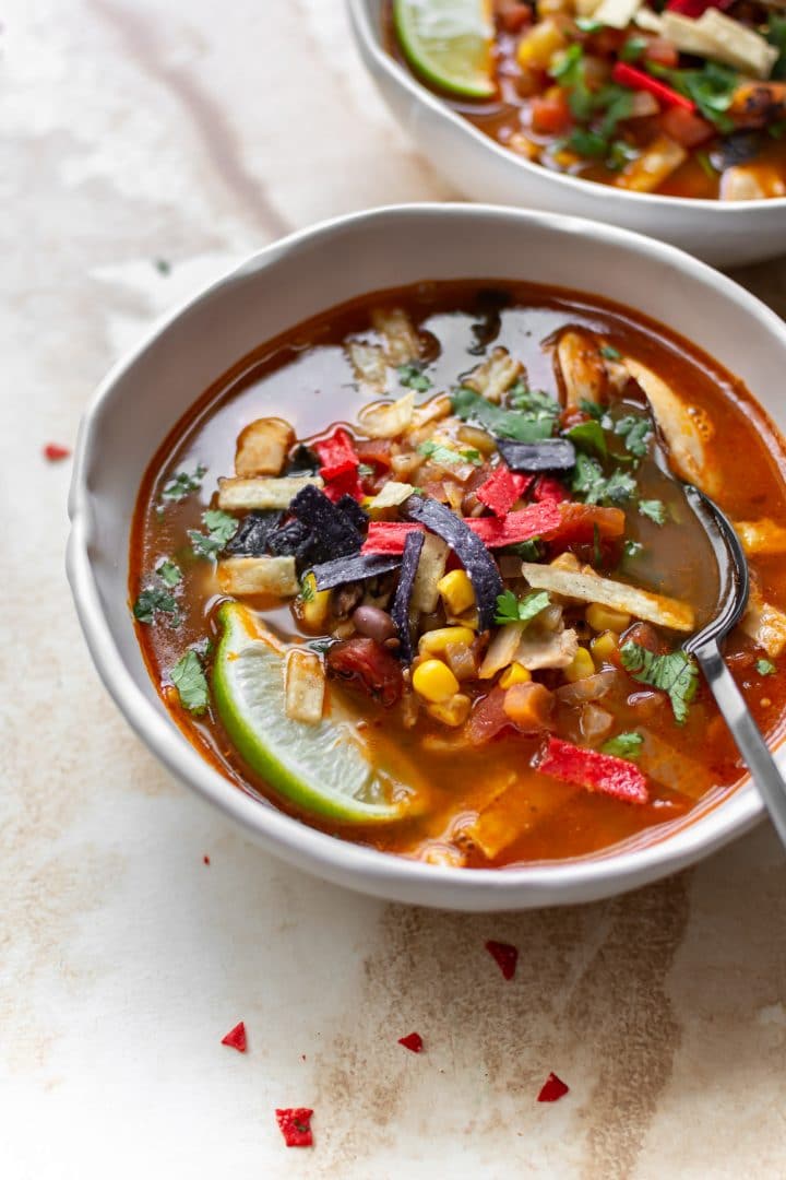 the BEST chicken tortilla soup (in two white bowls loaded with tortilla strips and other toppings)