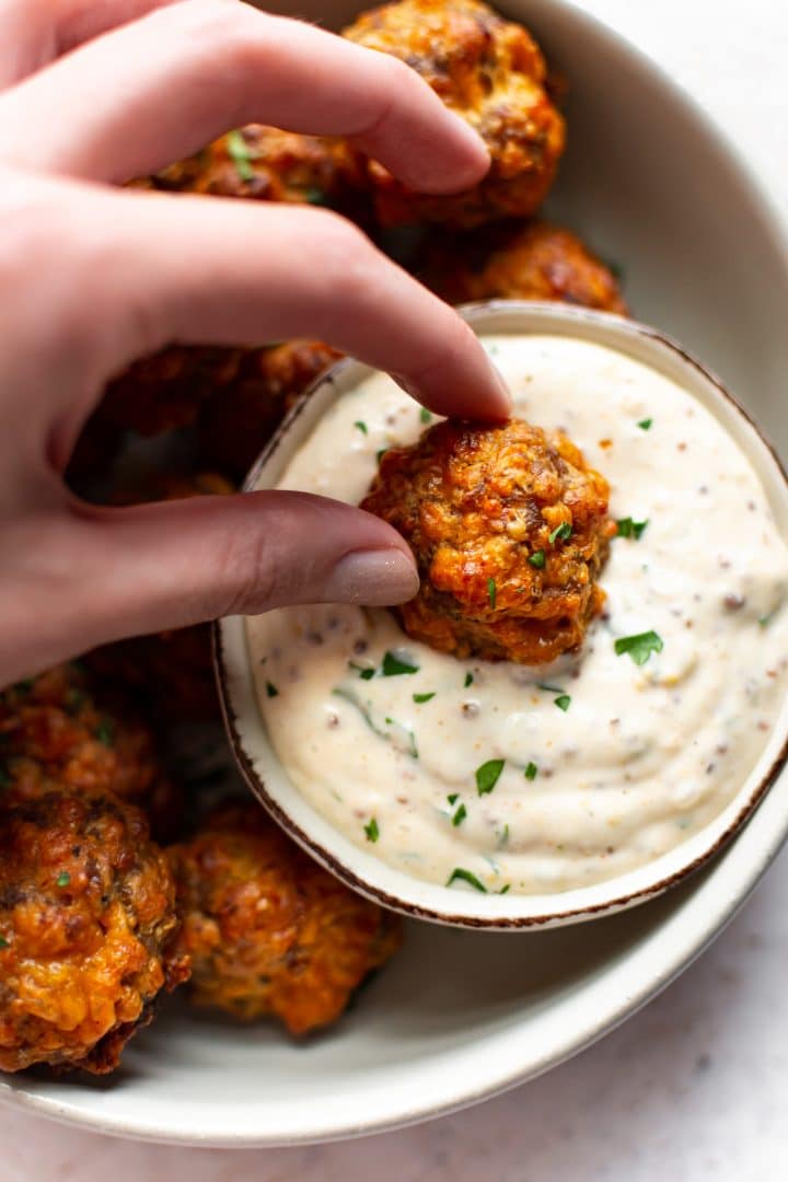 close-up of sausage ball being dipped in remoulade sauce