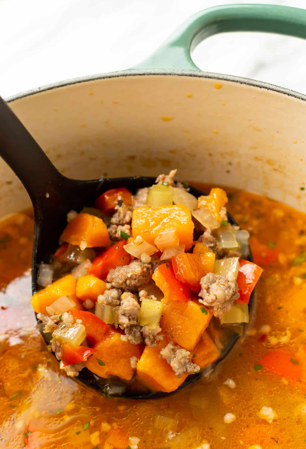 closeup of a soup pot with sausage and sweet potato soup with a ladle