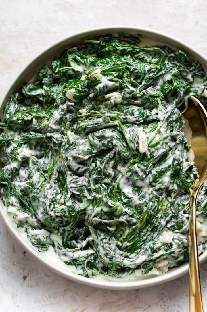 creamy spinach in a serving bowl with a gold serving spoon