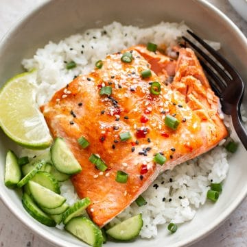 sweet chili glazed salmon in a bowl with rice, scallions, cucumber, lime, and sesame seeds