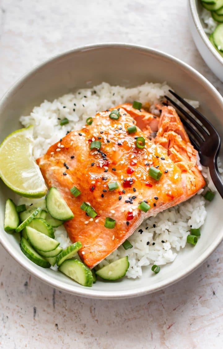 sweet chili glazed salmon in a bowl with rice, scallions, cucumber, lime, and sesame seeds