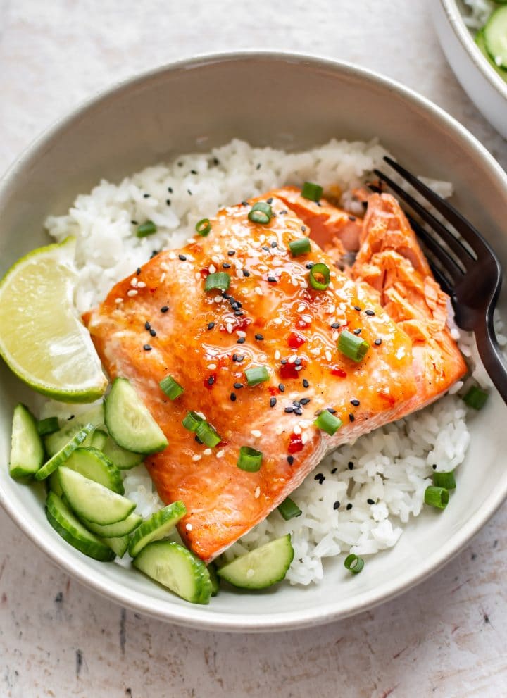 sweet chili glazed salmon in a bowl with rice, scallions, cucumber, lime, and sesame seeds