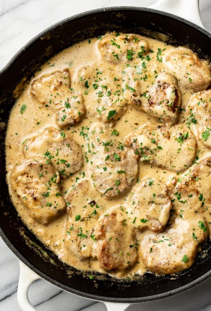 a cast iron skillet with pork tenderloin medallions in a creamy sauce