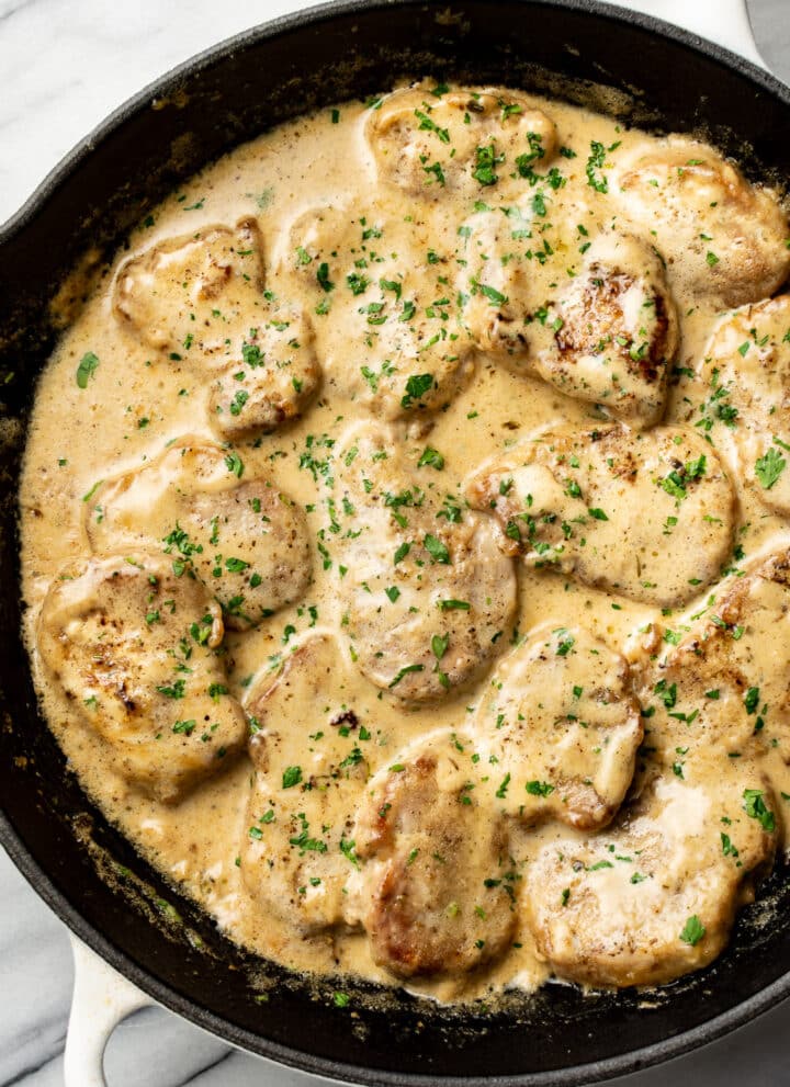 a cast iron skillet with pork tenderloin medallions in a creamy sauce