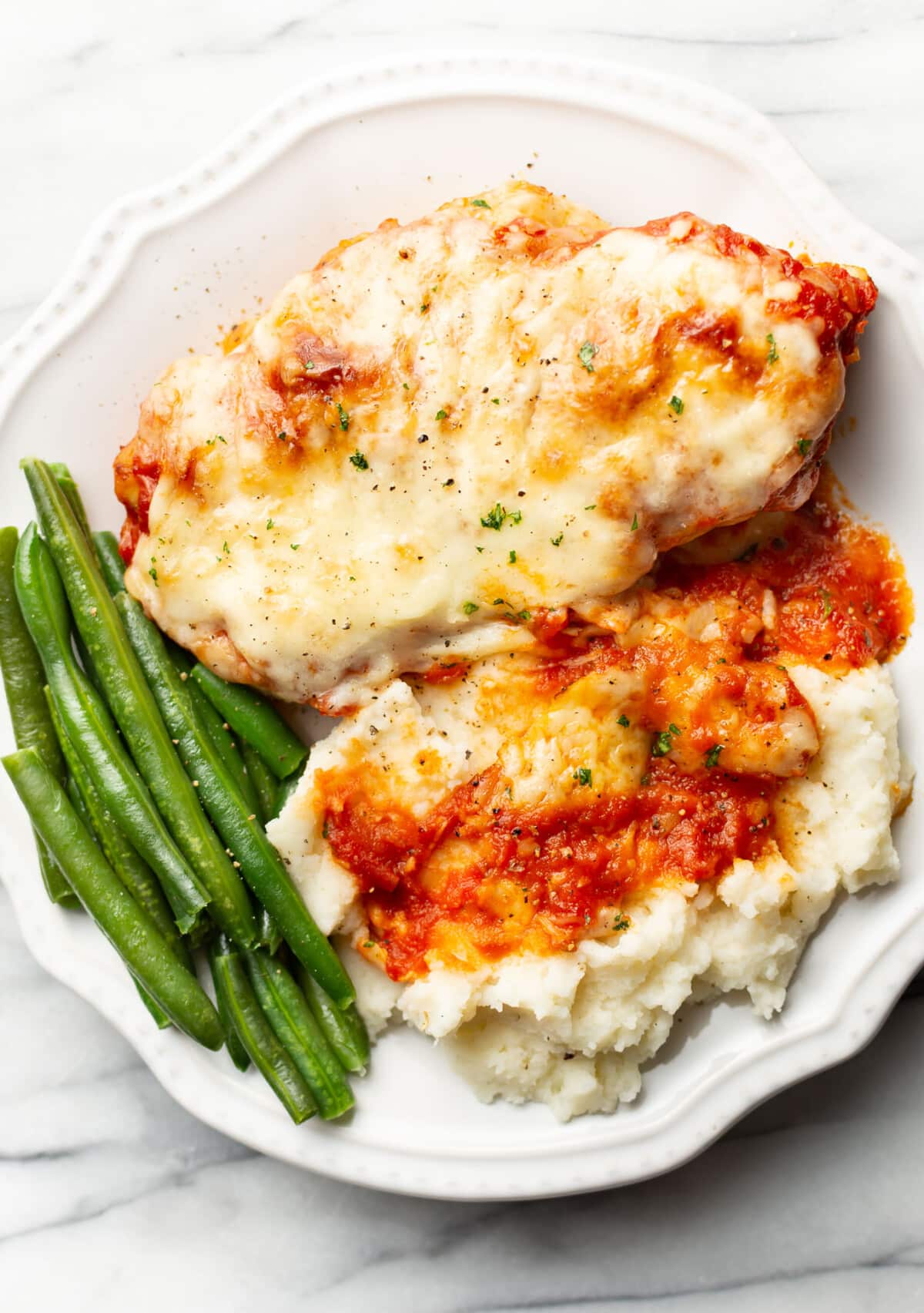 a plate with cheesy mozzarella chicken, green beans, and mashed potatoes
