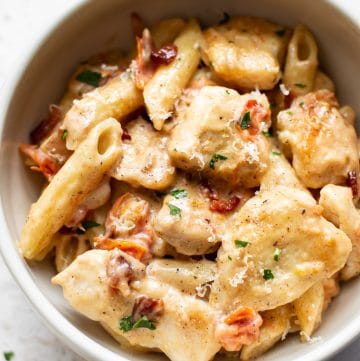creamy chicken penne with fresh tomatoes and bacon in a white bowl