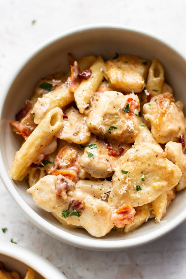 creamy chicken penne with fresh tomatoes and bacon in a white bowl