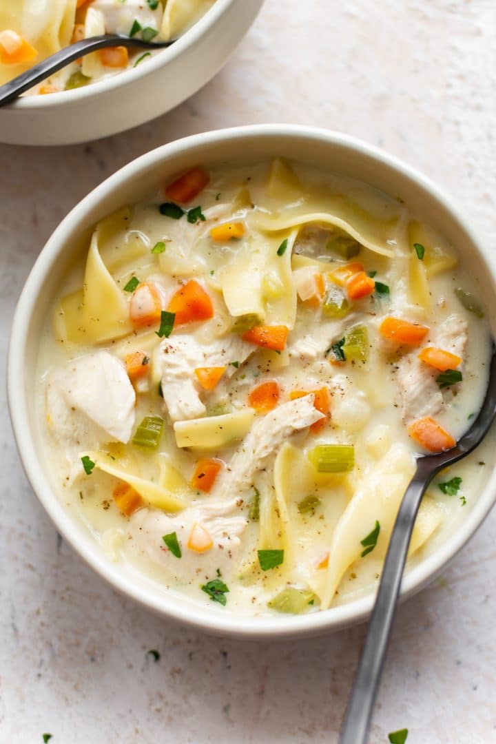 creamy chicken soup with egg noodles in two white bowls