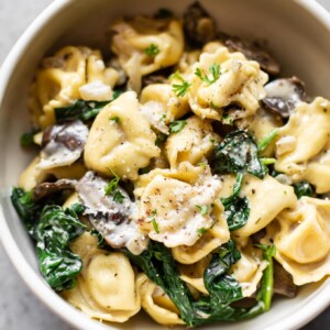 close-up of spinach tortellini with mushrooms in a white bowl