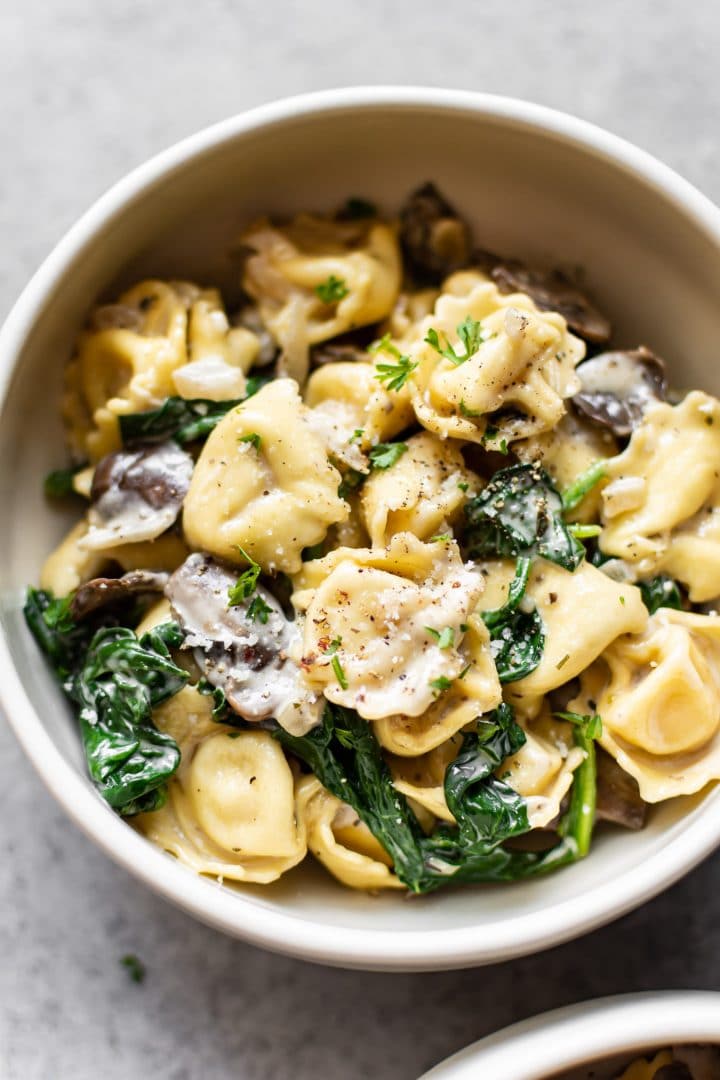 close-up of spinach tortellini with mushrooms in a white bowl