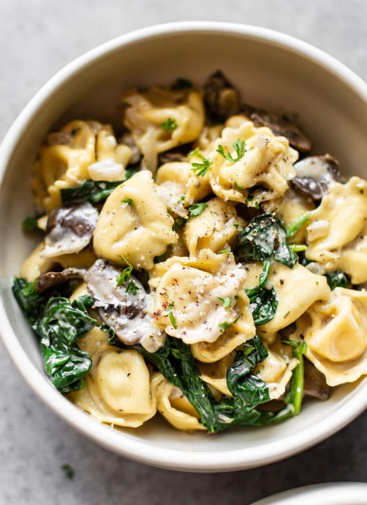 close-up of spinach tortellini with mushrooms in a white bowl