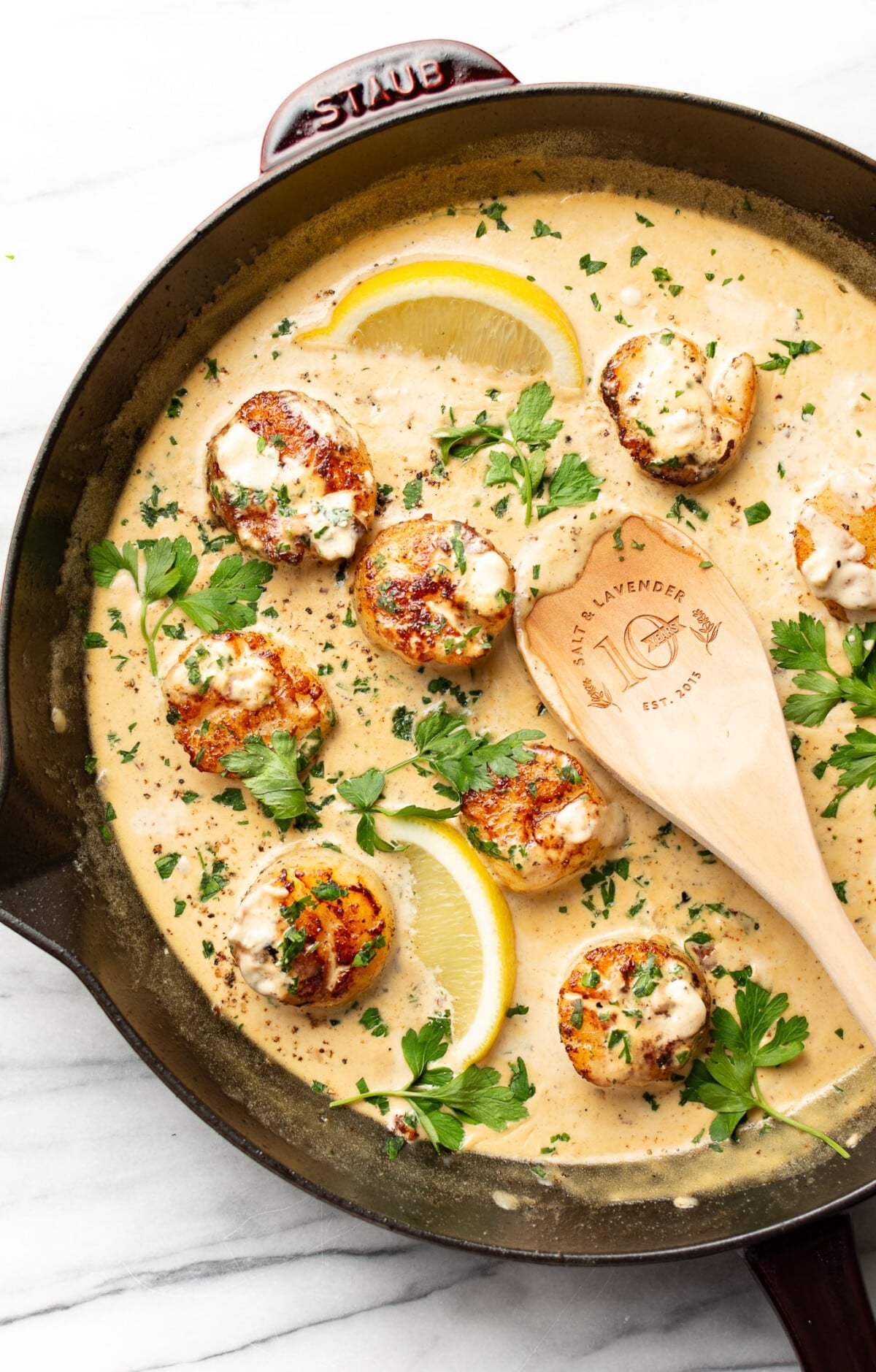 a skillet with creamy garlic lemon pan seared scallops and a wooden spoon