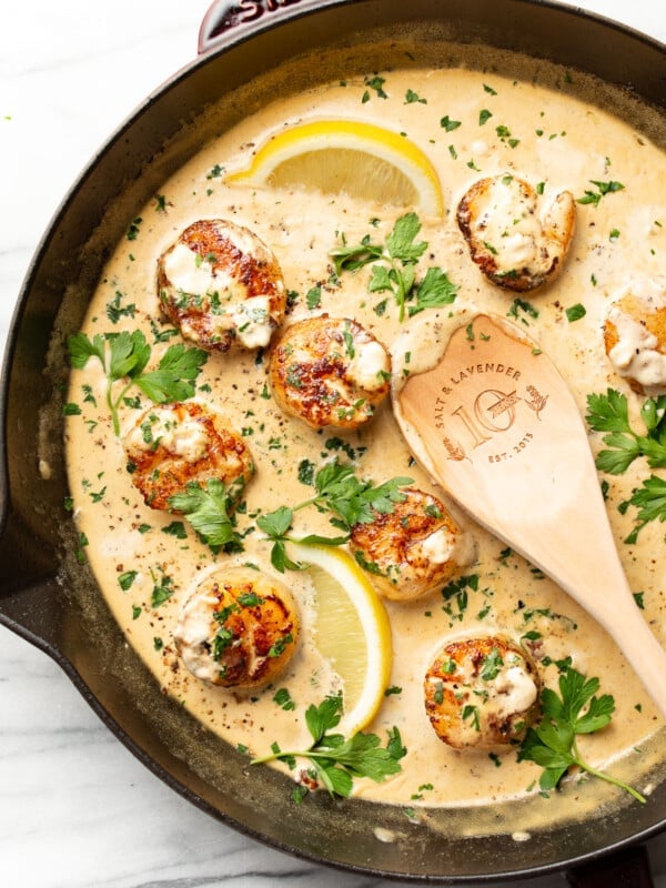 a skillet with creamy garlic lemon pan seared scallops and a wooden spoon