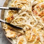 close-up of chicken fettuccine alfredo in a skillet being tossed with cooking tongs