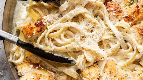 close-up of chicken fettuccine alfredo in a skillet being tossed with cooking tongs