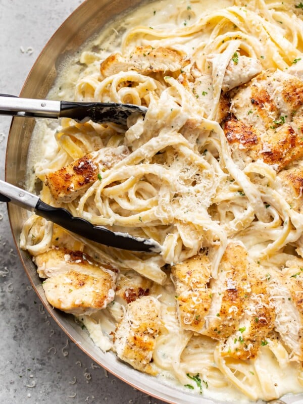close-up of chicken fettuccine alfredo in a skillet being tossed with cooking tongs