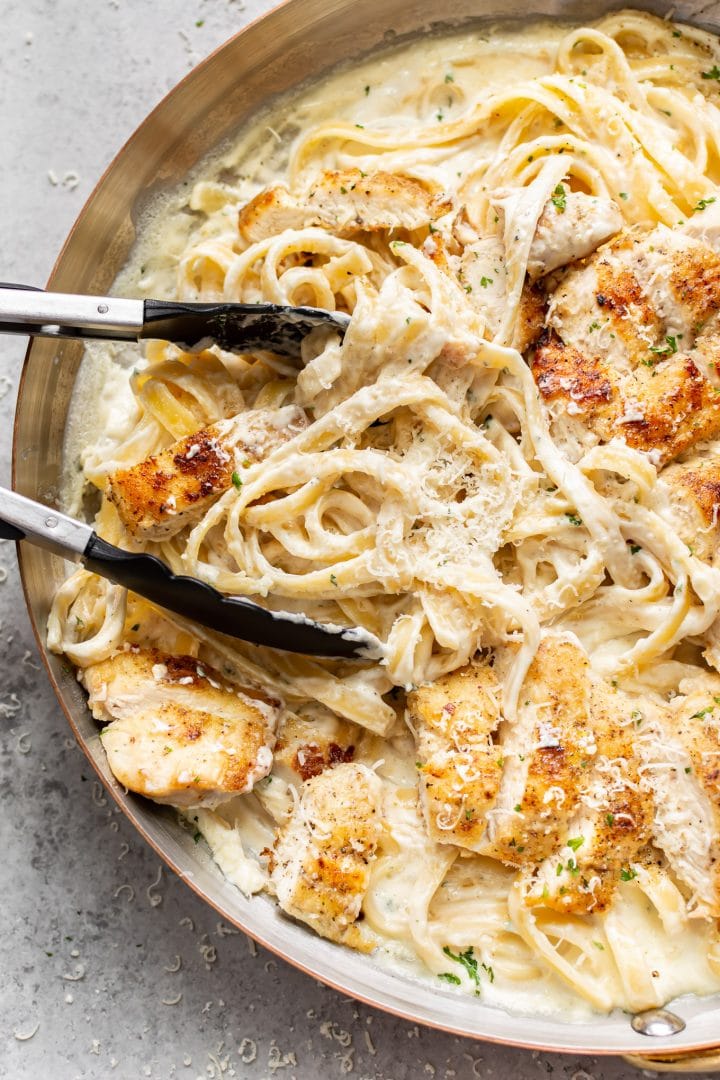 close-up of chicken fettuccine alfredo in a skillet being tossed with cooking tongs