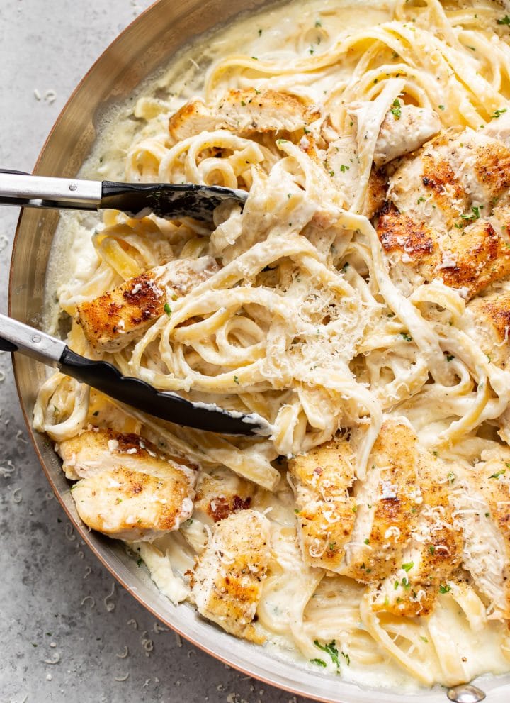 close-up of chicken fettuccine alfredo in a skillet being tossed with cooking tongs